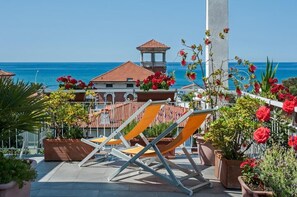A rooftop terrace with sun loungers, potted plants, and a view of the sea and buildings. - Hotel Scandinavia (Massa)