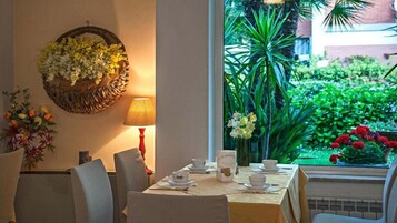 Un comedor con una mesa dispuesta para cuatro personas, un arreglo floral en la pared y vistas a un jardín exuberante a través de una ventana.