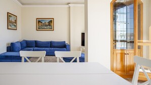 Ein Wohnzimmer mit einem blauen Sofa, weißen Sesseln, einem weißen Tisch und einem Holzschrank mit Glastüren.