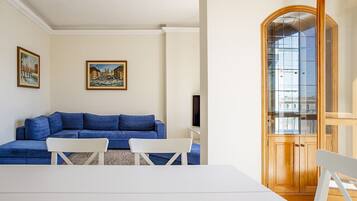 A living room with a blue sofa, white chairs, a white table, and a wooden cabinet with glass doors.