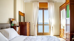 Ein Schlafzimmer mit einem großen Bett, einem Schminktisch, einem Spiegel und Blick auf das Meer durch ein großes Fenster.