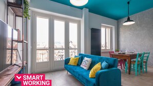 Una sala de estar moderna con un sofá azul, un escritorio de madera y una zona de comedor con mesa y sillas.