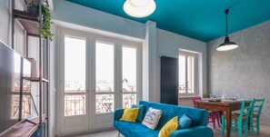 Ein modernes Wohnzimmer mit einem blauen Sofa, einem Holztisch und einem Essbereich mit Tisch und Stühlen.
