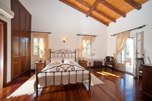 A bedroom with a wooden ceiling, a metal bed frame, a nightstand with a lamp, a chair, and a wardrobe.