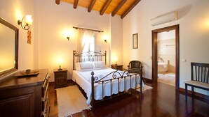 Een slaapkamer met een houten plafond, een bed met metalen frame, bedlampjes, een nachtkastje, een stoel en uitzicht op de badkamer.
