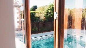 Une vue à travers une fenêtre sur une piscine, avec une terrasse en bois et une clôture en arrière-plan.
