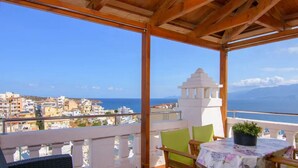 Varanda com mesa e cadeiras, com vista para o horizonte costeiro e o mar.