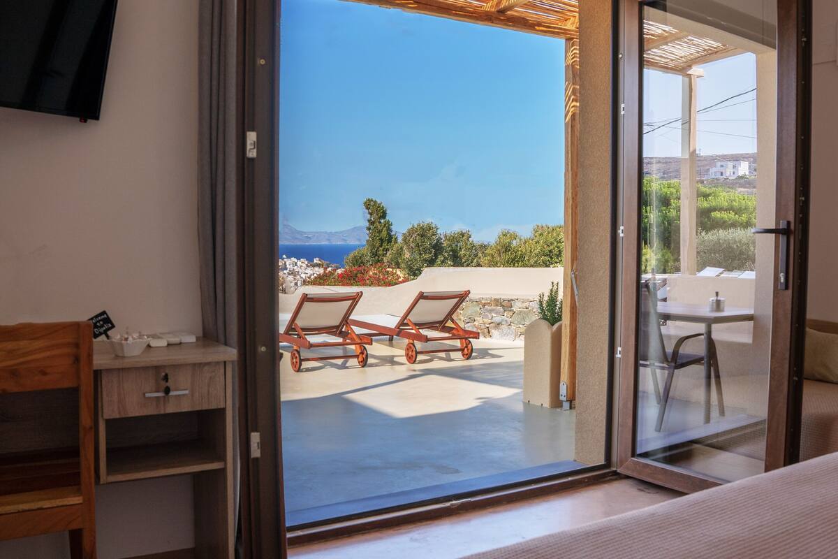 Une pièce dotée d’une porte-fenêtre coulissante donnant sur un espace extérieur aménagé avec deux fauteuils de jardin en bois et une table.
