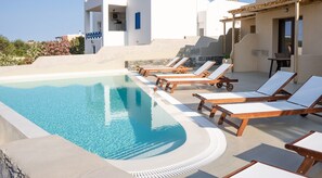 A pool area with lounge chairs and a clear blue pool. - Dipolis Apartments (Syros)
