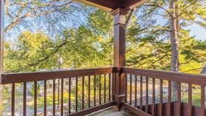 A wooden deck with a railing, overlooking a residential area with trees and houses.