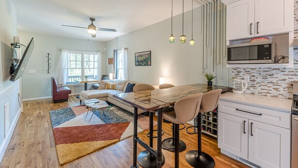 A modern kitchen with white cabinets, a stainless steel microwave, and a wooden dining table with bar stools.