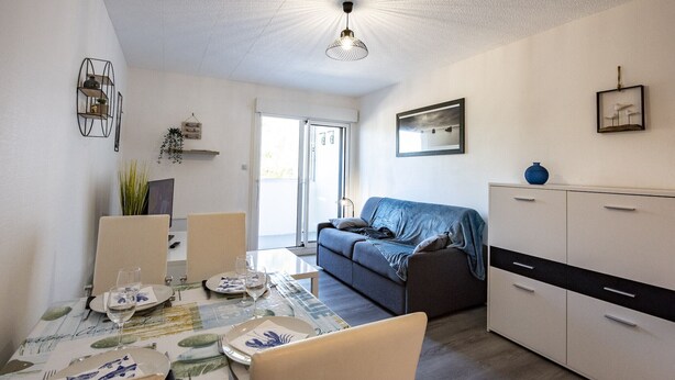 A modern living room with a dining area, a sofa, a cabinet, and a door leading to an outdoor area. - Becs Beach 500m away - Apartment for 4 (Saint-Hilaire-de-Riez)