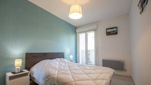 A bedroom with a bed, bedside lamps, a window, and a radiator. - Becs Beach 500m away - Apartment for 4 (Saint-Hilaire-de-Riez)