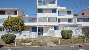 A two-story residential building with a blue door, white exterior, and a small front yard with a tree and a bush. - Becs Beach 500m away - Apartment for 4 (Saint-Hilaire-de-Riez)