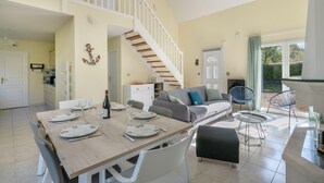 A dining area with a wooden table set for four, a staircase leading to an upper level, and a seating area with a sofa and chairs.