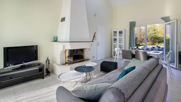 A modern living room with a flat-screen TV, fireplace, sofa, and dining area with a view.