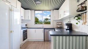 Una cocina moderna con armarios blancos, encimera negra y ventana con vistas a palmeras.