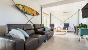 Una sala de estar moderna con un sofá de cuero marrón, dos sillones, una mesita y una decoración de tabla de surf en la pared.