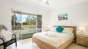 Un dormitorio con cama, mesitas de noche, una silla, un balcón y vistas al exterior.