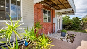 Una casa con fachada de ladrillo, terraza de madera y diversas macetas con plantas.