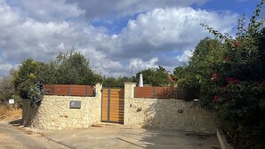 A gated entrance with a stone wall and a wooden gate, surrounded by greenery and a clear sky. - Crete, 2 houses together for 2 families (kefalas)
