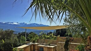 A patio with a table and chairs, a stone wall, and a view of snow-capped mountains. - Crete, 2 houses together for 2 families (kefalas)