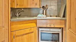 A compact kitchen with wooden cabinets, a stainless steel range hood, a built-in oven, and a sink. - Lake District village apartment with private riverside hot tub (Coniston)