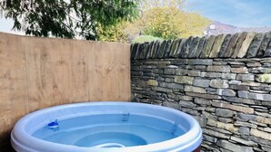 A hot tub in a wooden enclosure with a stone wall background. - Lake District village apartment with private riverside hot tub (Coniston)