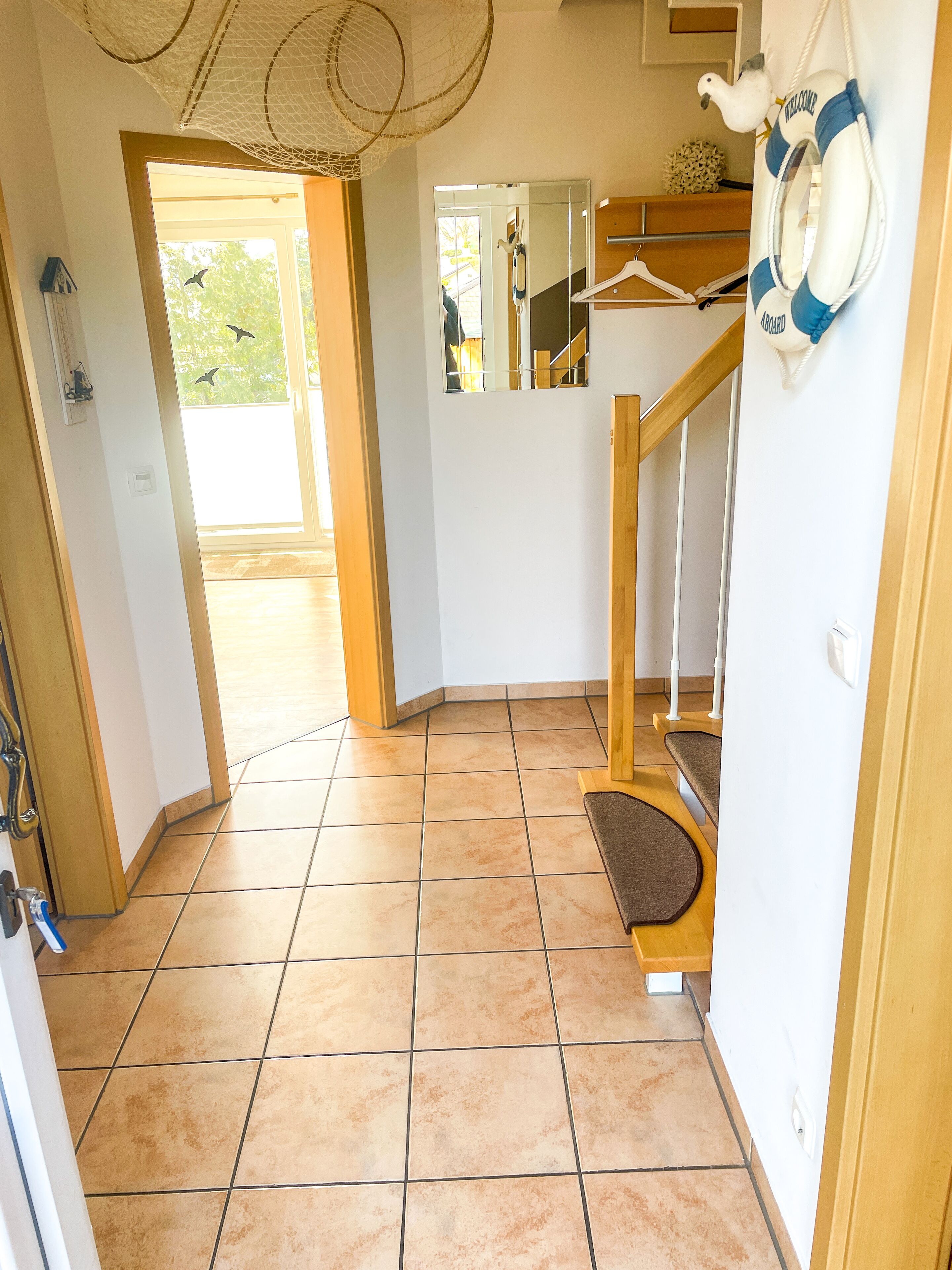A room with a wooden staircase, a mirror, and a life preserver on the wall.