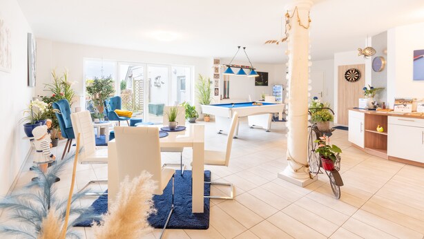 A modern living room with a dining area, a pool table, and a kitchen.