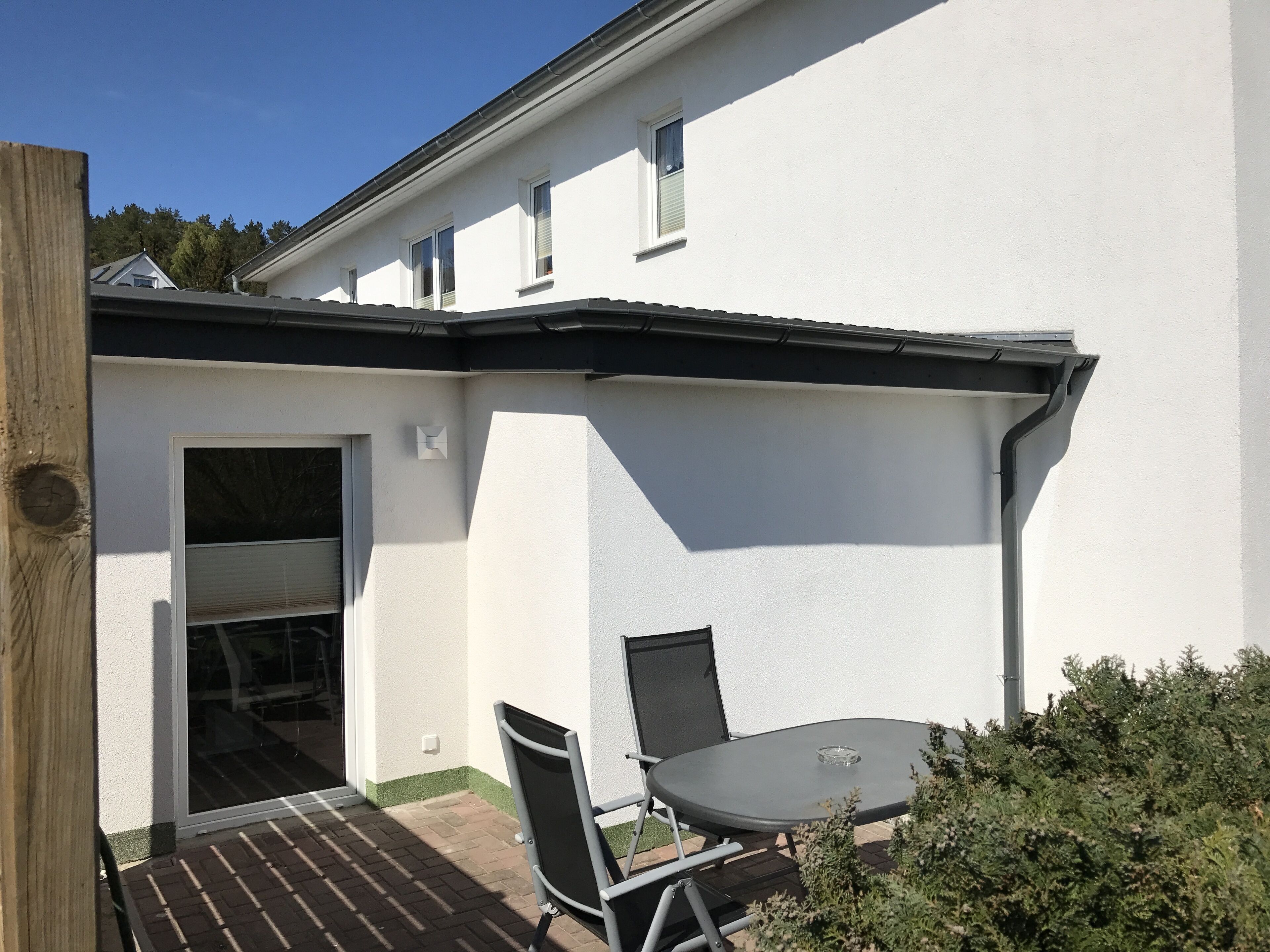 A white building with a patio area featuring a table and chairs, a door, and a window.