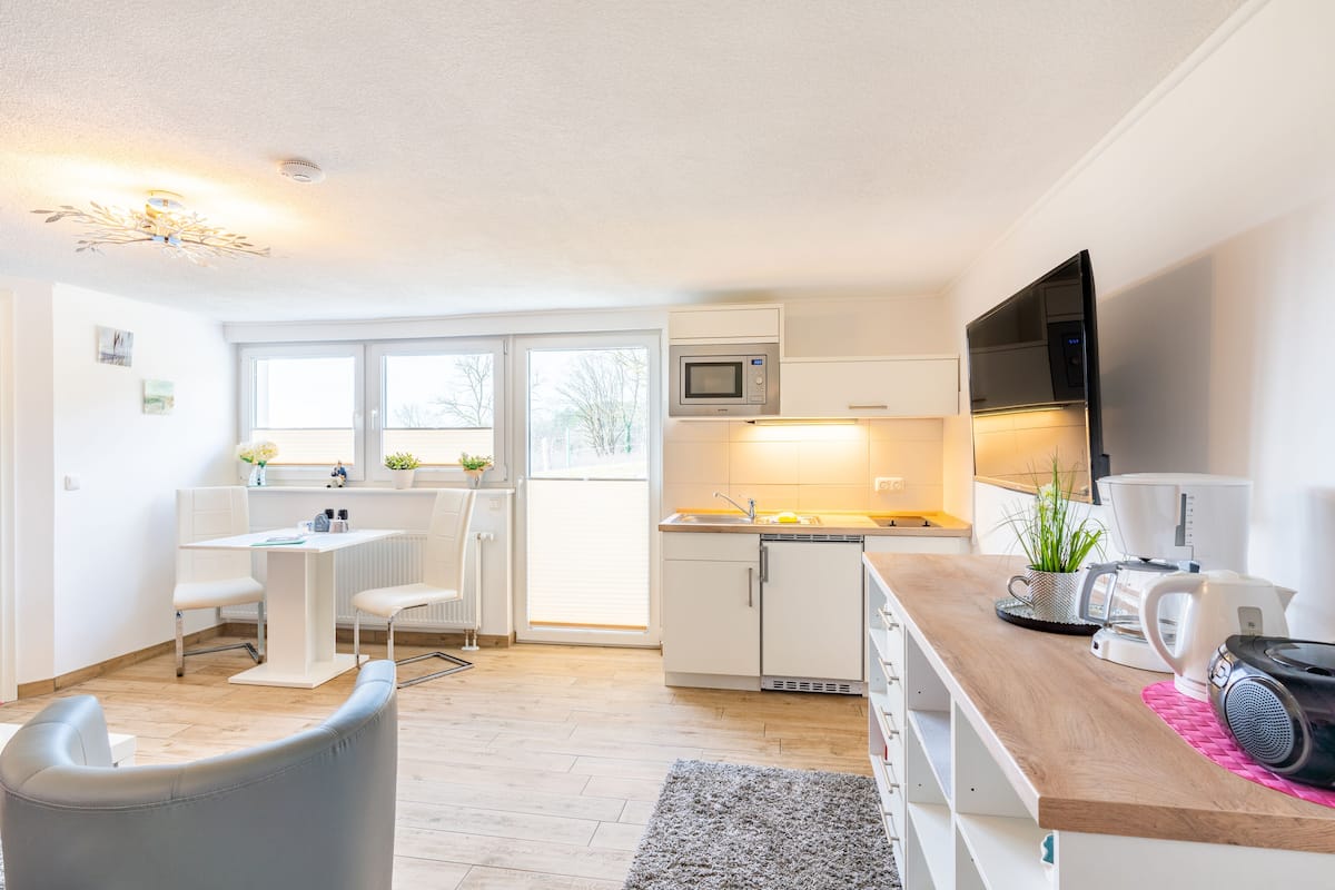 A modern kitchen with white cabinetry, a wooden countertop, a microwave, a coffee maker, and a television.