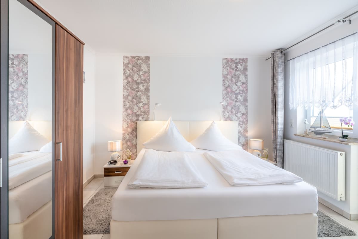 A hotel room with a large bed, two bedside tables with lamps, a mirror, and a window with curtains.
