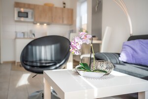Una sala de estar moderna con una mesita de centro blanca, una silla negra y un sofá con un cojín morado.