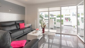 A modern living room with a black leather sofa, a white coffee table, and a large sliding glass door leading to an outdoor patio.
