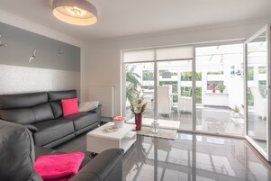 Una sala de estar moderna con un sofá de cuero negro, una mesa de centro blanca y un amplio ventanal corredera que da a un patio exterior.