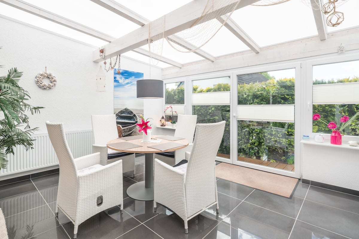 A bright, spacious patio with a dining table and chairs, large windows, and a view of greenery.