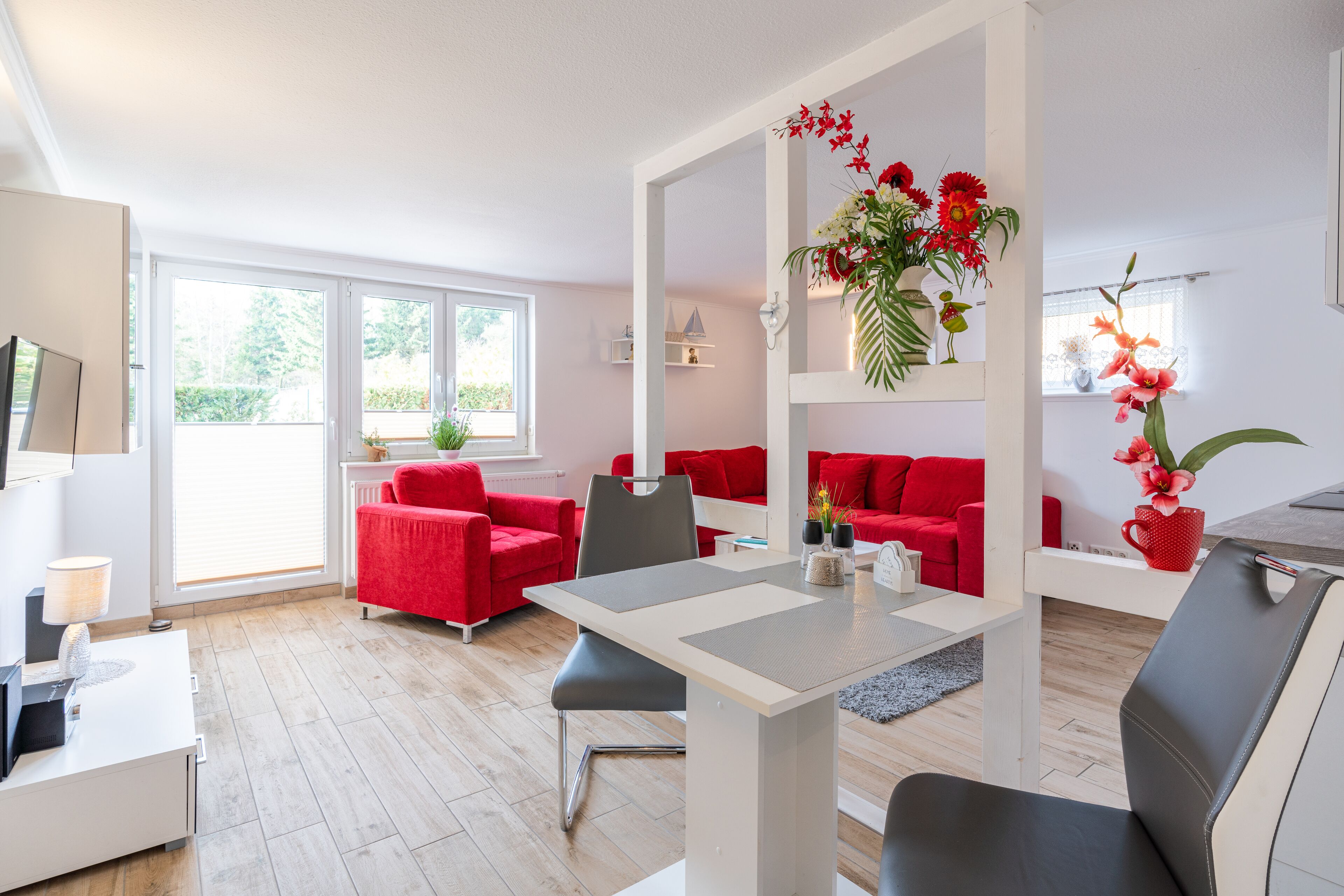 A modern living room with red sofas, a dining table, and a kitchen area.
