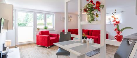 A modern living room with red sofas, a dining table, and a kitchen area.