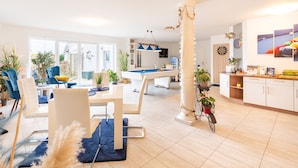 A modern living room with a pool table, a dining area with chairs, and a kitchen area with cabinets and a countertop.