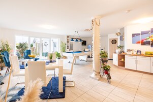 Una sala de estar moderna con mesa de billar, comedor con sillas y área de cocina con armarios y encimera.