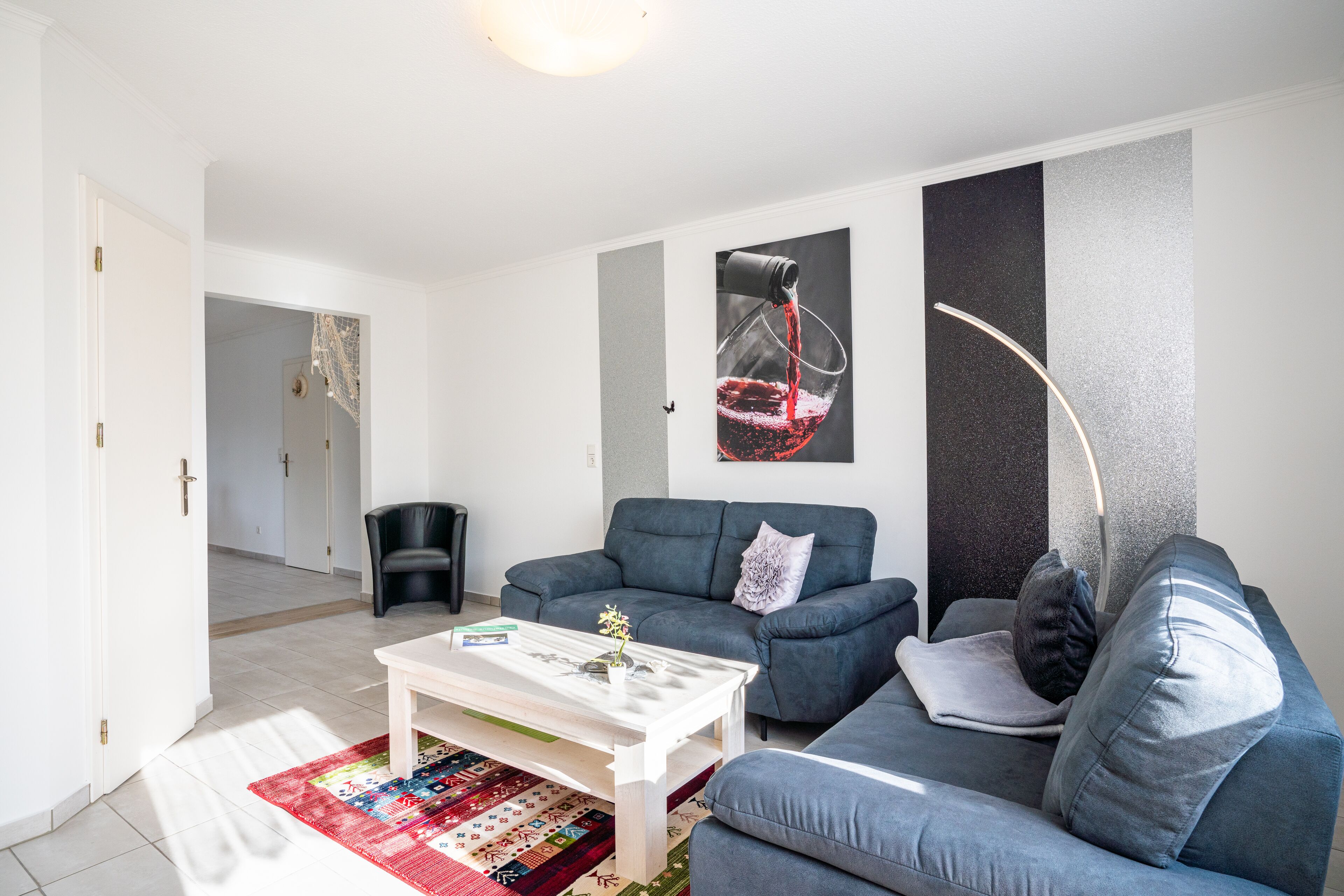Ein modernes Wohnzimmer mit einem grauen Sofa, einem weißen Couchtisch und einem farbenfrohen Teppich.
