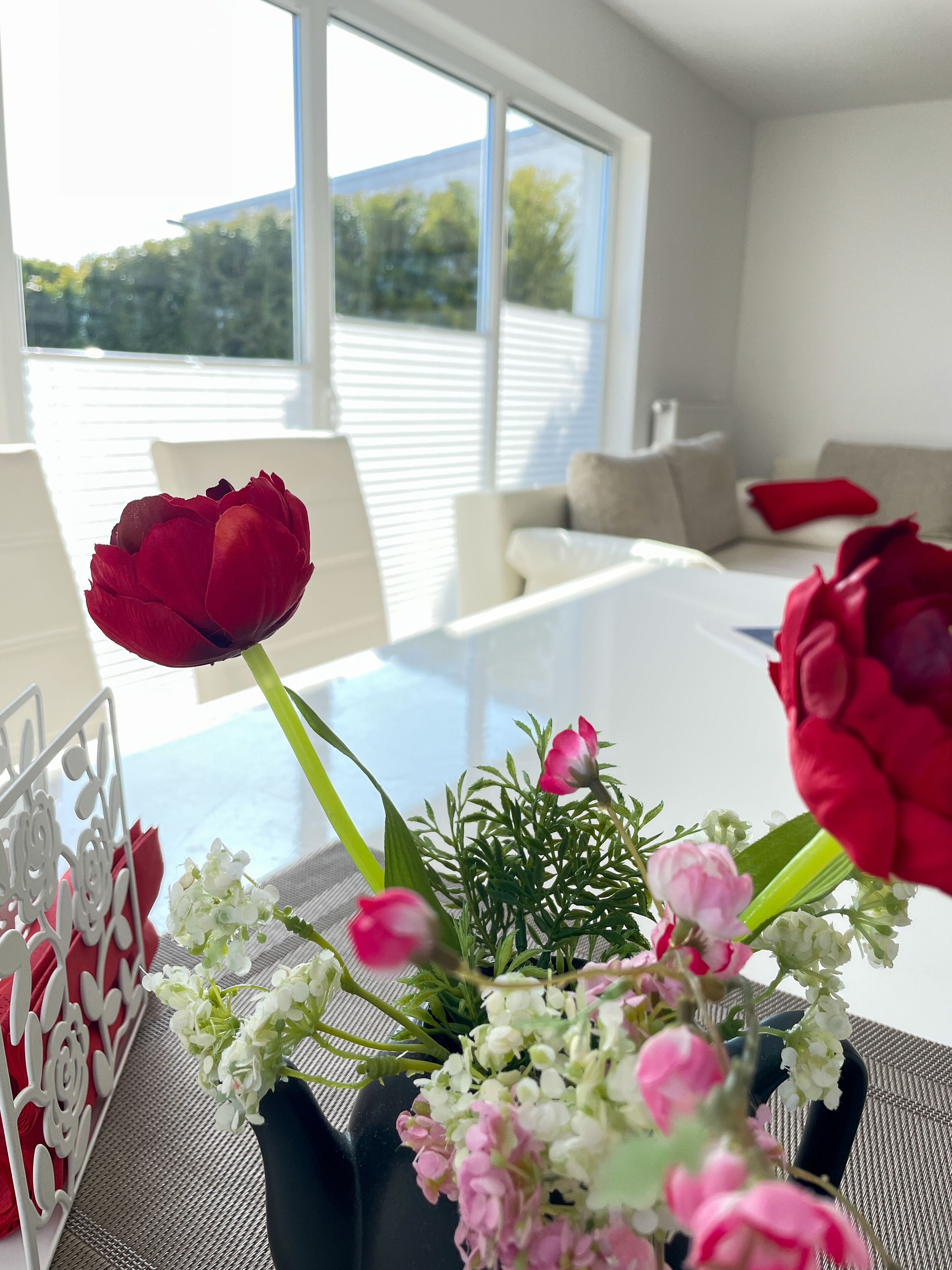 A dining table with a floral centerpiece, white chairs, and a view of a building through large windows.