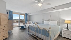 Un dormitorio con cama con dosel, ventilador de techo, mesita de noche y vistas a la ciudad a través de amplias ventanas.