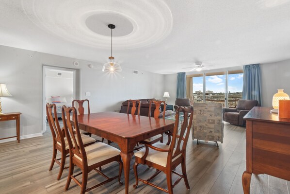 A dining area with a wooden table and chairs, a sofa, and a view of the outdoors.