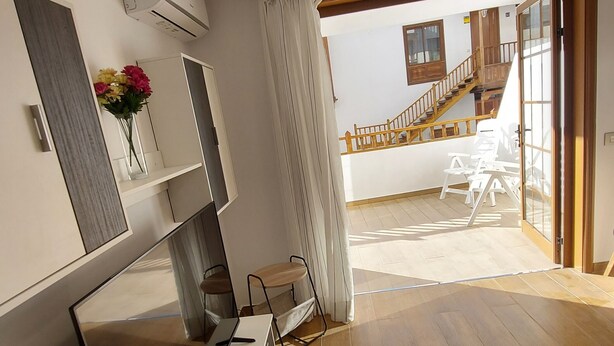 A modern interior with a wooden floor, a white desk with a computer, a chair, and a vase of flowers. A staircase leads to an upper level with a balcony. - Los Gigantes NEW apartment , 2 bedrooms (Acantilados de Los Gigantes)