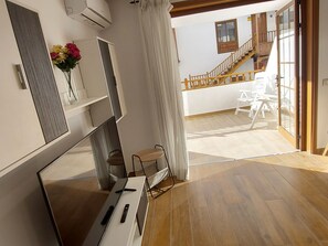 Un intérieur moderne avec un plancher en bois, un bureau blanc avec un ordinateur, une chaise et un vase de fleurs. Un escalier mène à un niveau supérieur avec un balcon.