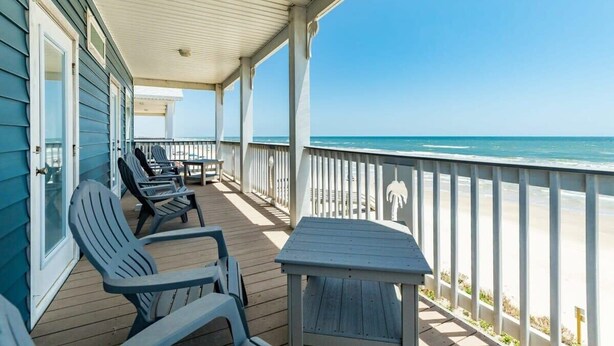 Un espace extérieur abrité, doté de chaises et d’une table, avec vue sur une plage.