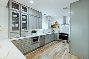 A modern kitchen with grey cabinets, stainless steel appliances, and a wooden floor.