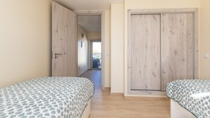 A bedroom with two beds, wooden wardrobes, and a view to the outside.